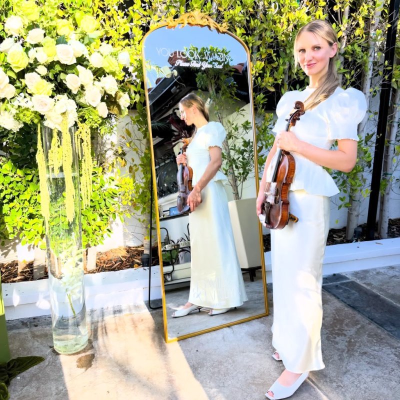 Mila with her violin beside a floral gold mirror