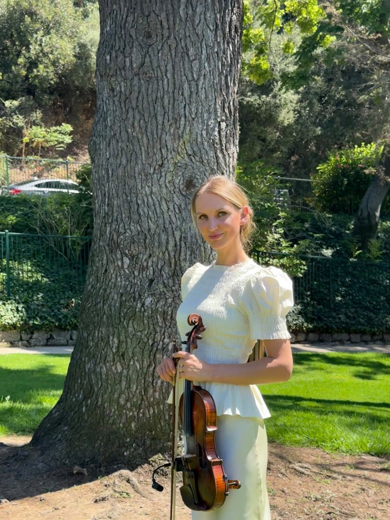 Mila with her violin in the shade of a garden tree
