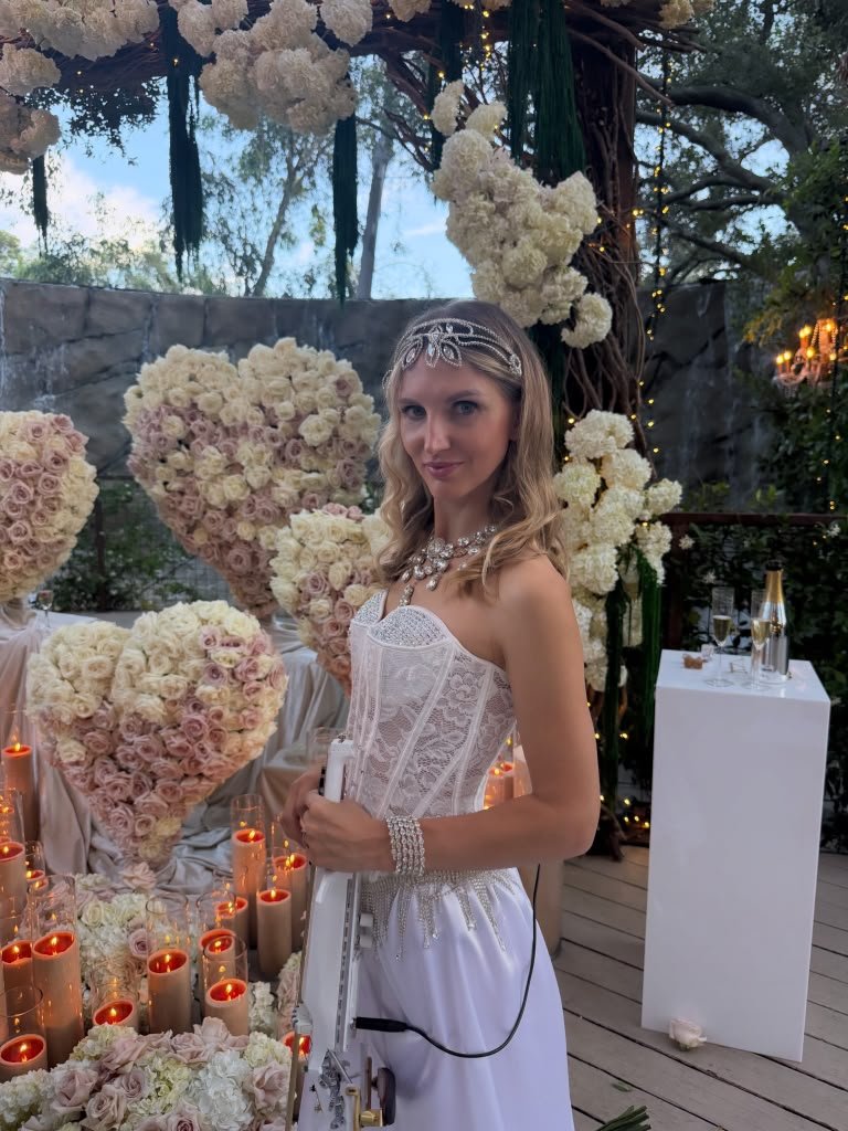 Live violin by a floral arch lit with candles